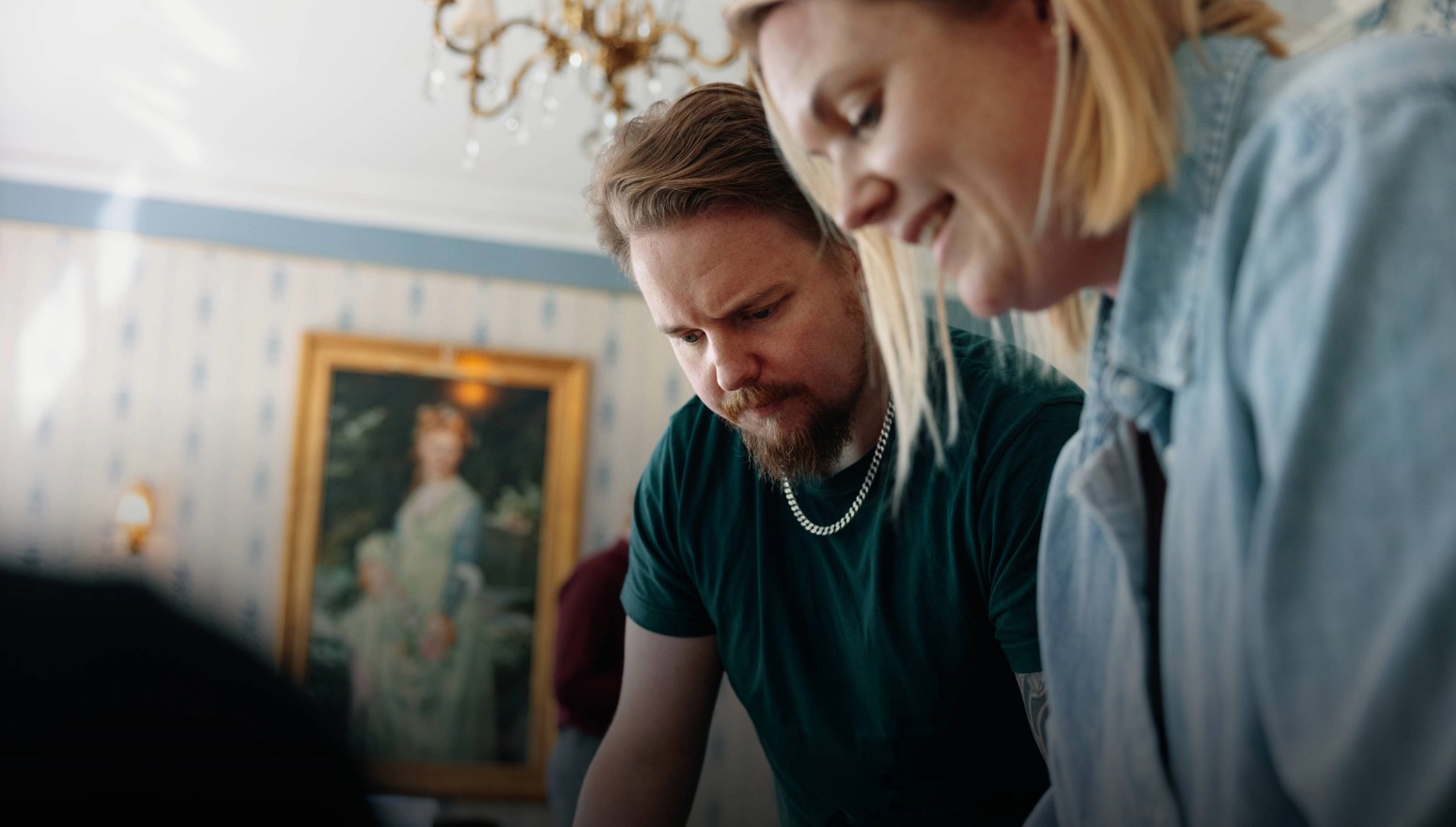 En man och en kvinna står i ett rum, böjer sig framåt och tittar ner på samma sak.