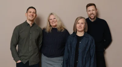 Två män och två kvinnor mot en rosa vägg, De tittar in i kameran och ler.