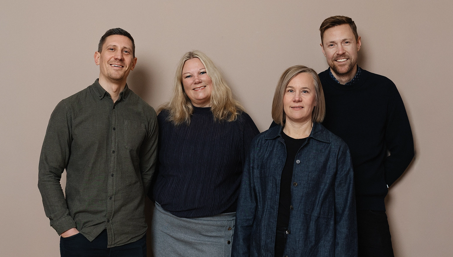 Två män och två kvinnor mot en rosa vägg, De tittar in i kameran och ler.