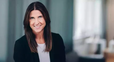 Kvinna med mörkt hår och kavaj tittar in i kameran och ler.